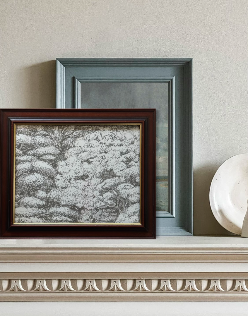 Two framed artworks on a decorative shelf with a neutral background