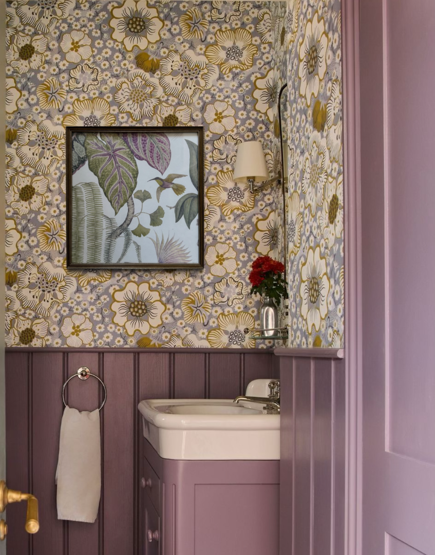 Lilac bathroom with pretty vintage gold framed wall decor, floral wallpaper, purple paneling and a sink.