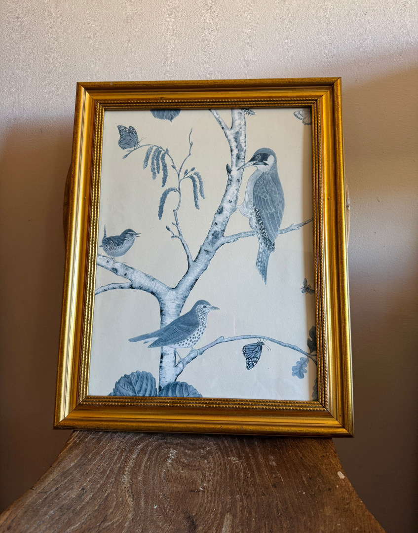 Framed artwork with birds on a branch against a beige background placed on antique wood chair seat