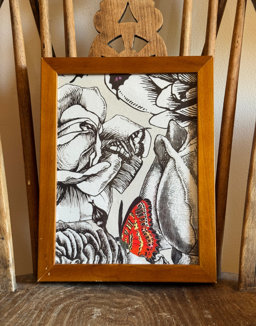 Centrally placed vintage framed eclectic wall decor of roses and nutterflies on an antique wooden chair seat with spindle design