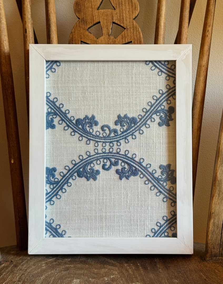 Pretty and fresh white and blue embroidered textile in white wood frame placed on seat of an antique wooden chair