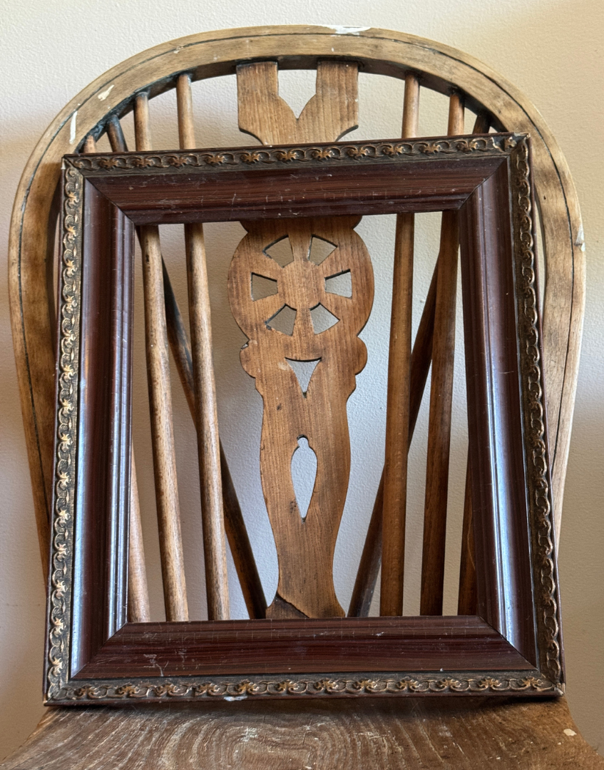 Vintage empty wood picture frame with decorative metal corners and dark antique finish.