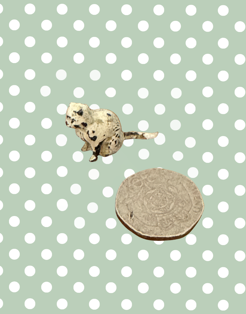 miniature white playworn sitting Britains cat lead figure next to a twenty pence piece coin for scale