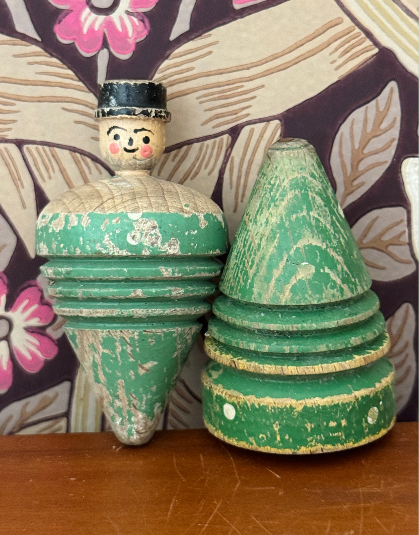 Pair of antique wooden spinning tops styled on a wooden shelf against William Morris Pimpernel wallpaper, featuring a carved gentleman and painted polka dot design.