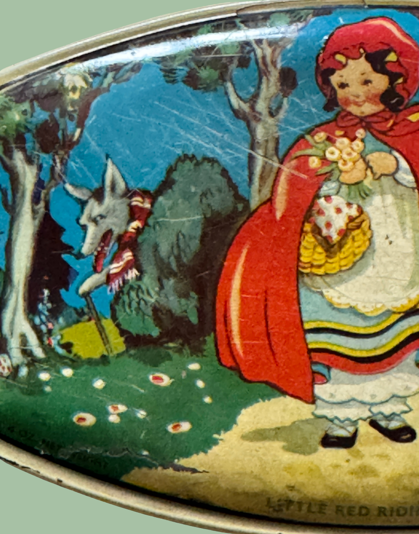 Close up left side of 1930s Little Red Riding Hood advertising tin showing wolf illustration, woodland path and flower detail on lid artwork