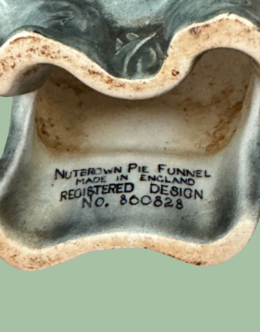 Close-up of the inside of a ceramic pie funnel with printed text reading 'Nuterown Pie Funnel Made in England Registered Design No. 860828' on a pale green background.