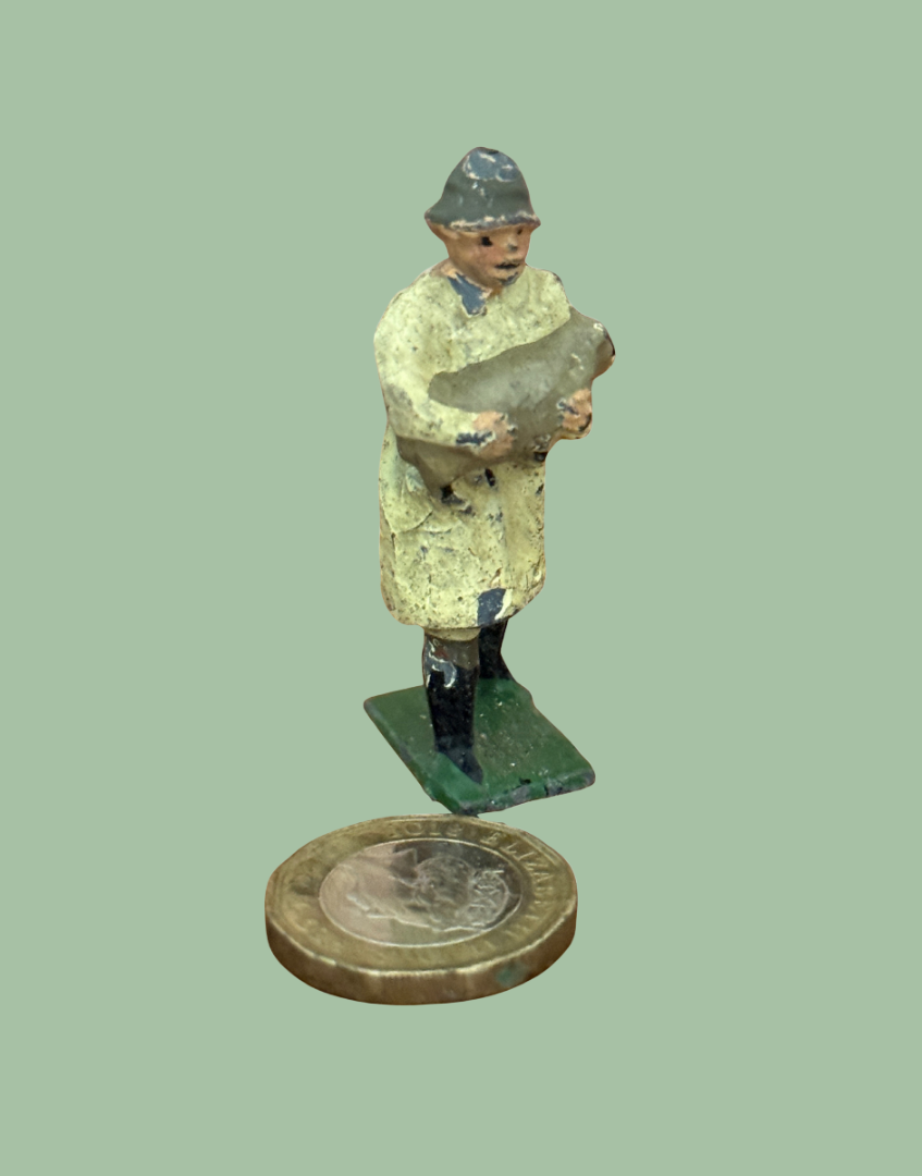traditionally dressed britains farmer in coat, boots and hat carrying a lamb next to a one pound coin for scale