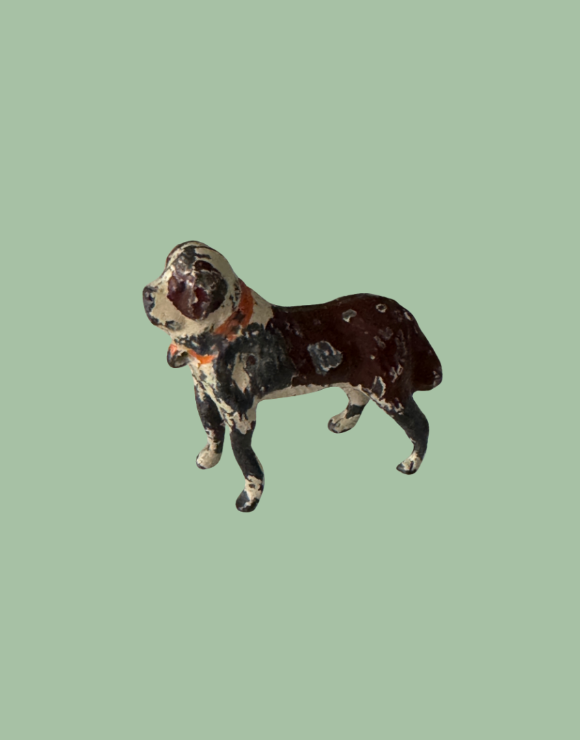 A vintage cast iron dog figurine with a distressed, peeling dark brown and black paint finish, set against a solid sage green background.