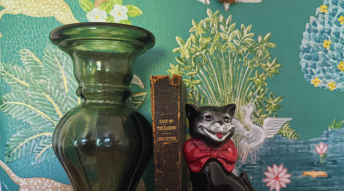 A trio of eclectic home decor collectables including an  antique leather black book, quirky black cat figurine and green glass candle holder