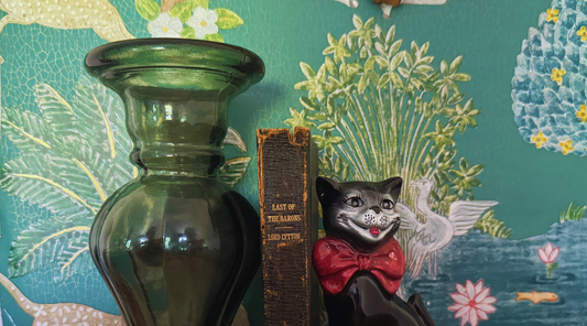 A trio of eclectic home decor collectables including an  antique leather black book, quirky black cat figurine and green glass candle holder