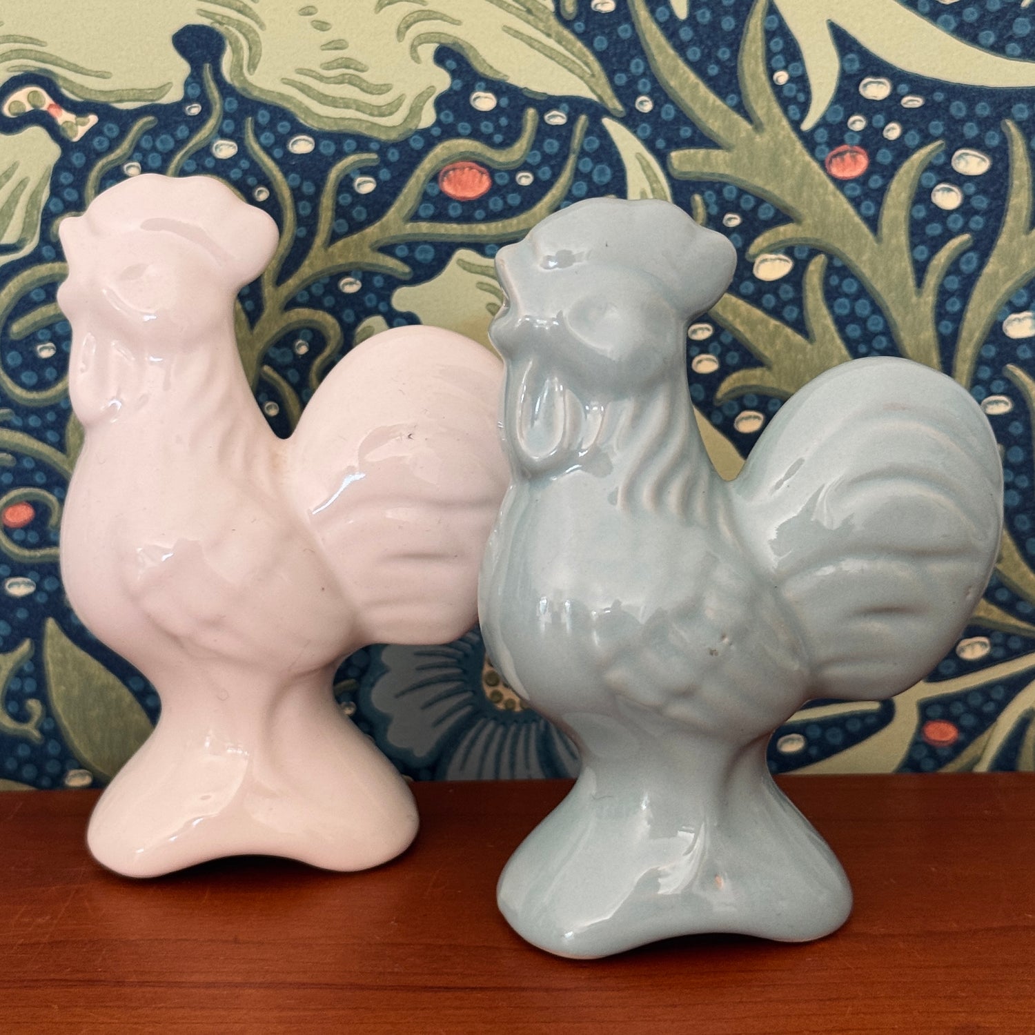 A pair of white and blue vintage cockerel shaped pie birds against William Morris Seaweed wallpaper background