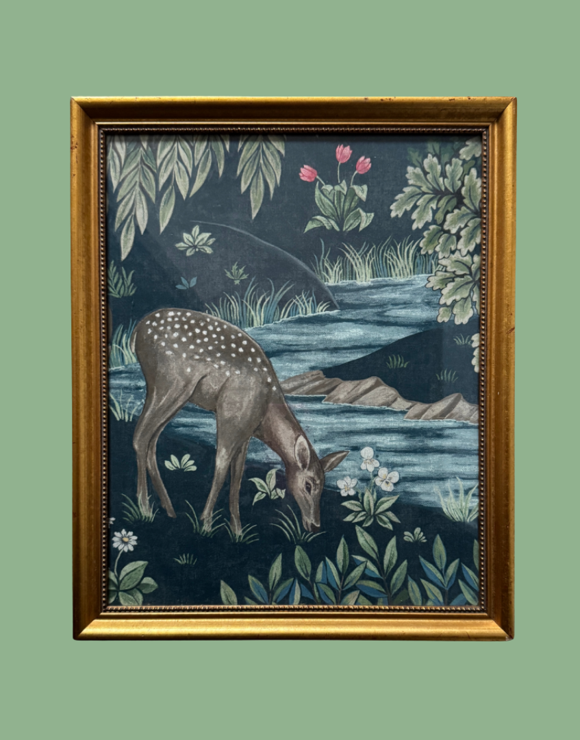 A framed William Morris art print depicting a spotted deer grazing by a river, with a dark blue background and green foliage, enclosed in a gold frame.