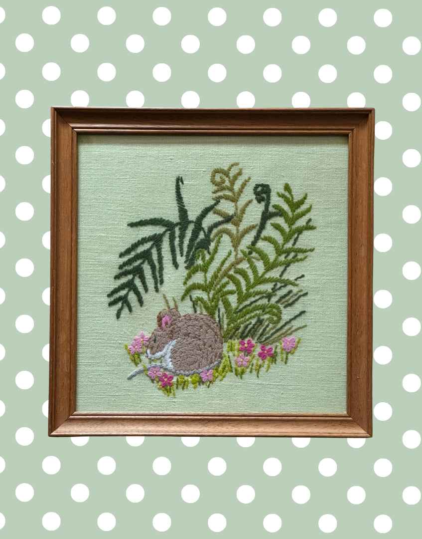 Close up of embroidered sleeping country mouse surrounded by pink floral detail and textured stitching