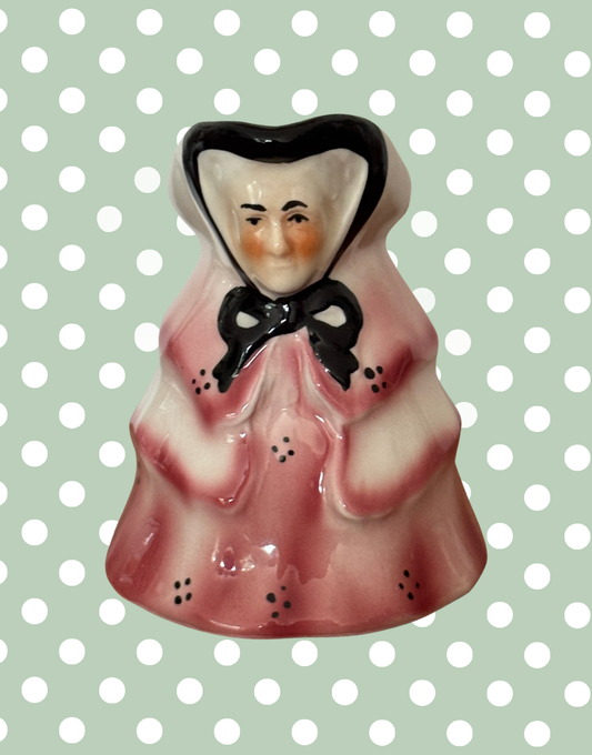 Small ceramic milk jug of a an old lady in a pink dress with a black bow 