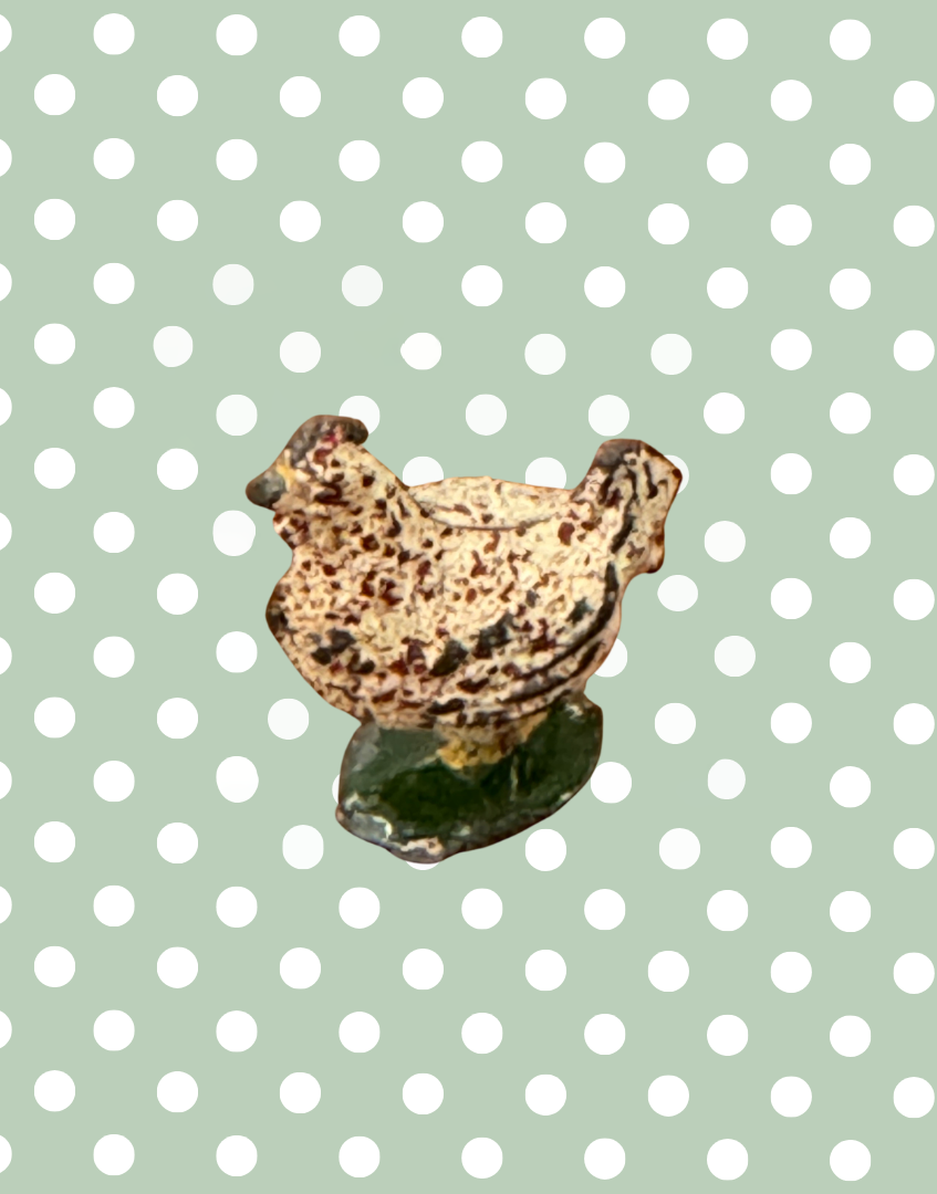 Small lead chicken figurine on a green background with white polka dots