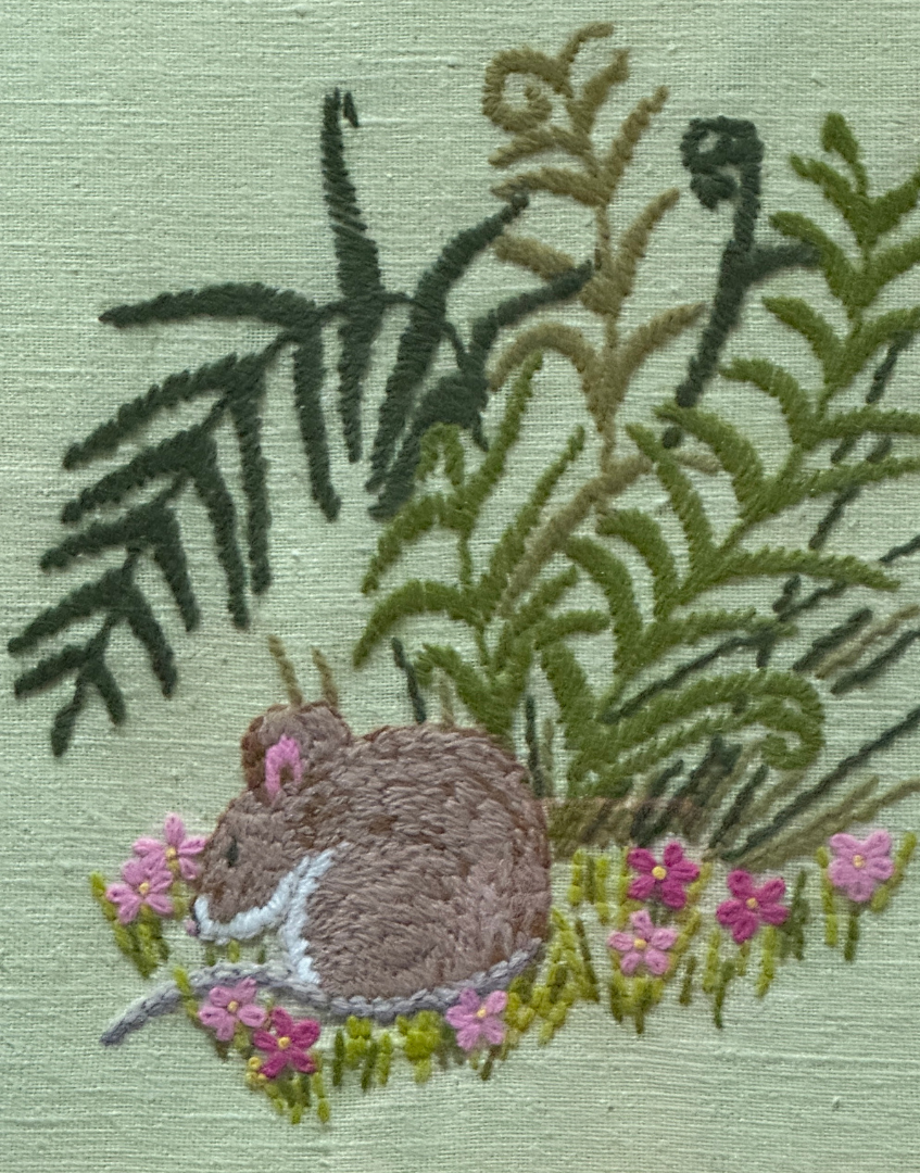 Close up of embroidered sleeping country mouse surrounded by pink floral detail and textured stitching