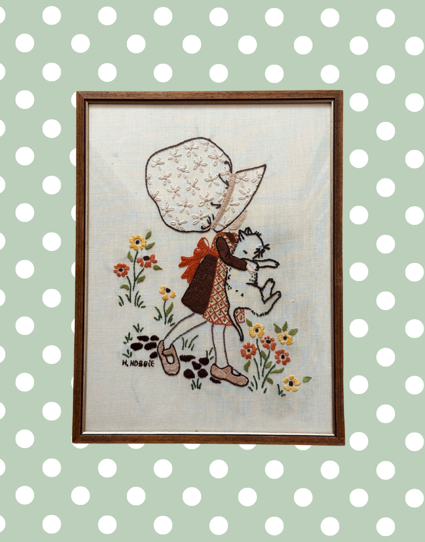 Vintage Hollie Hobbie framed embroidery featuring girl holding white cat with floral background.