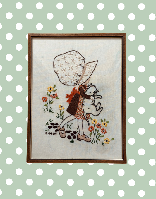 Vintage Hollie Hobbie framed embroidery featuring girl holding white cat with floral background.