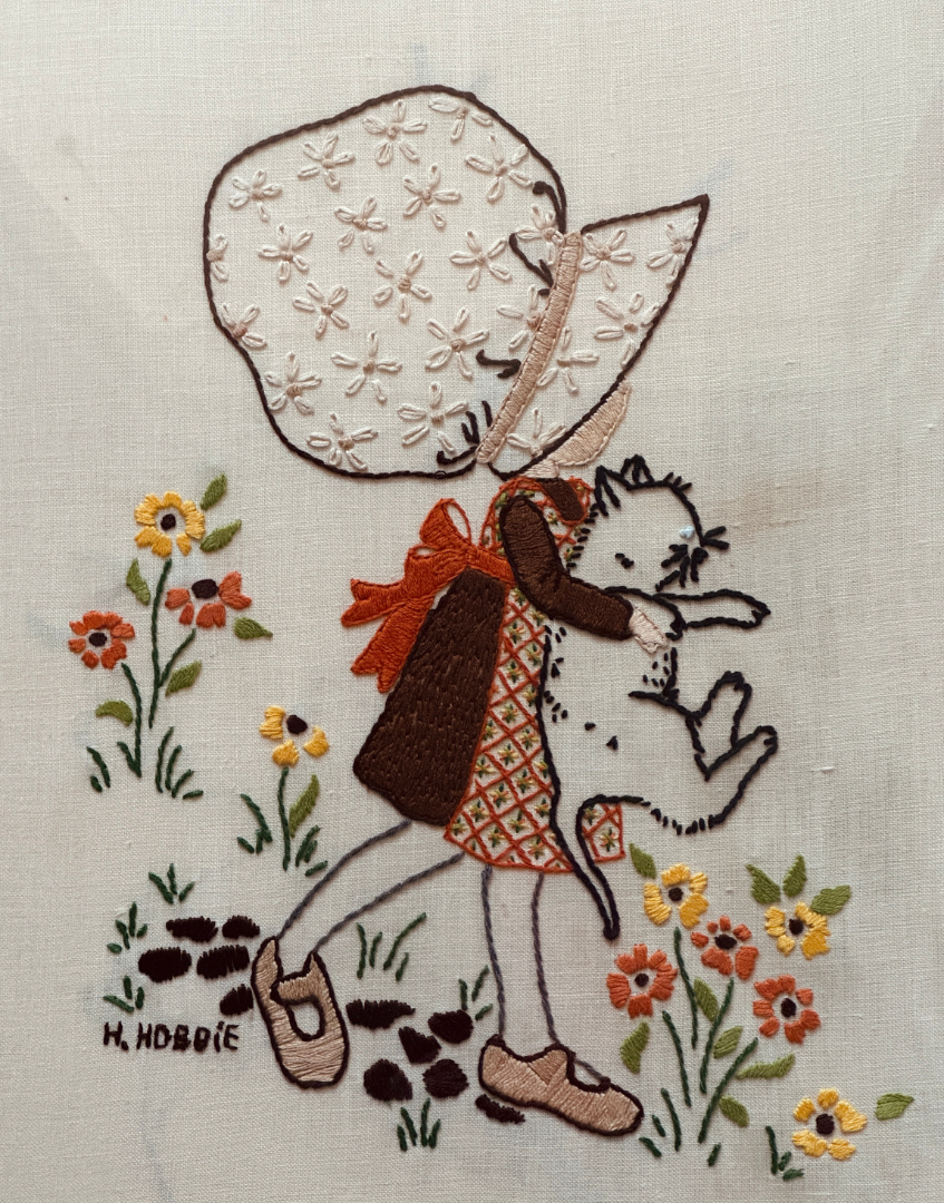 Close up of Hollie Hobbie embroidery showing brown and orange dress and white cat detail.