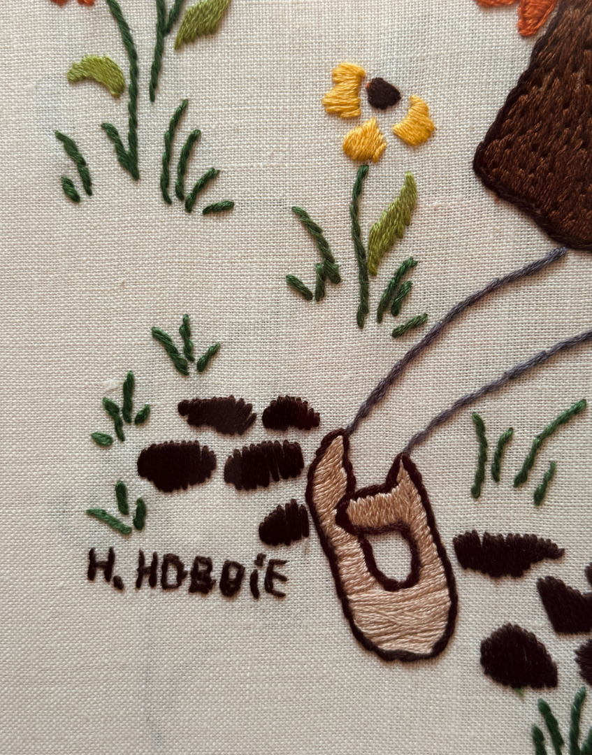 Embroidered design of a shoe, plants, and 'H. Hoboe' branding on fabric.