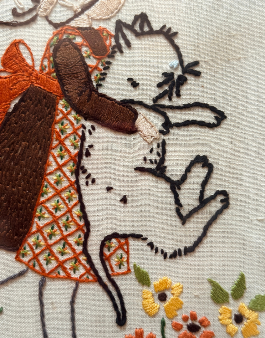 Close up of Hollie Hobbie embroidery showing close up of holding a white cat with orange and yellow flowers