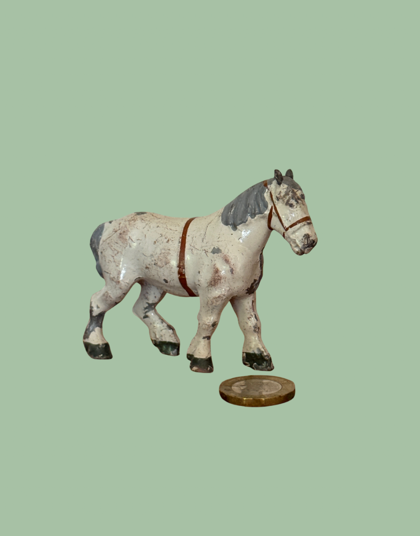 A small painted horse figurine or model shown against a flat light green background, with a round coin placed below it for scale.