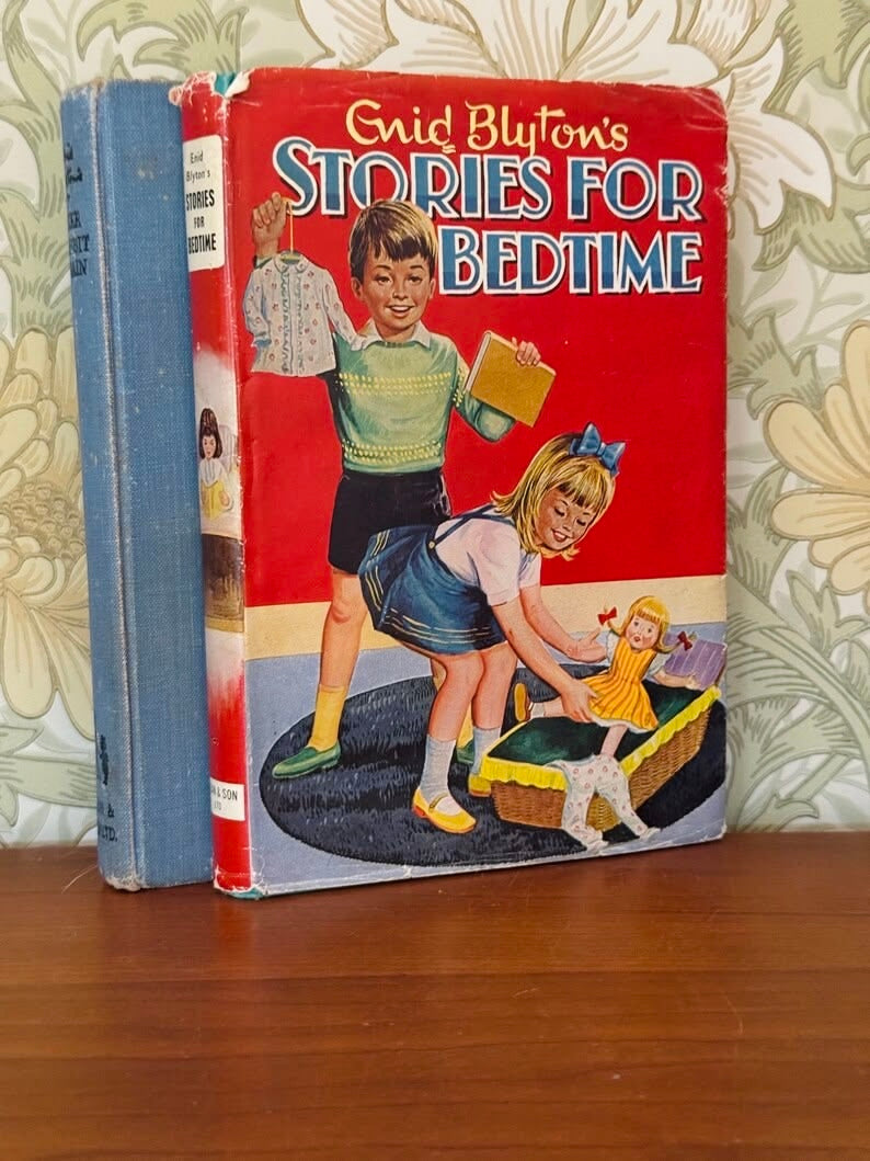 Vintage hardcover children's book titled "Enid Blyton's Stories for Bedtime" standing on a wooden surface against a floral wallpaper background. The front cover is bright red with illustrated children and large white title text outlined in blue.