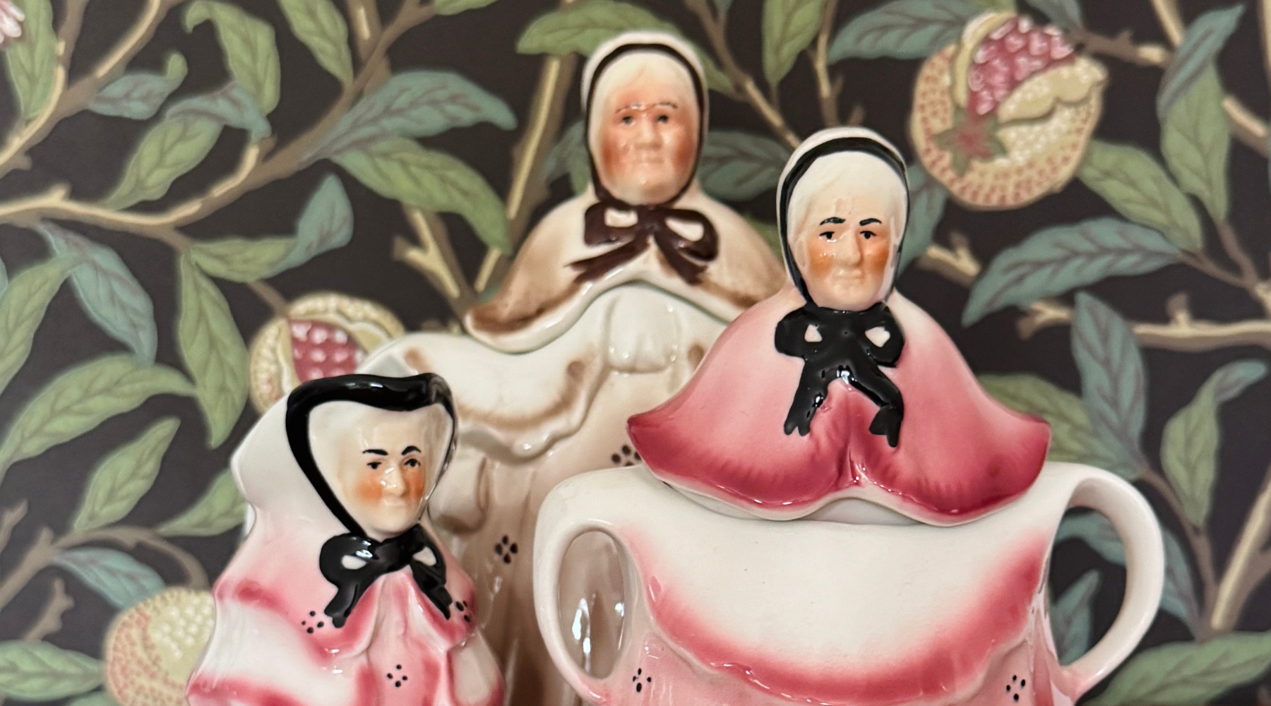 Three ceramic figures in traditional attire with a teapot on a decorative background