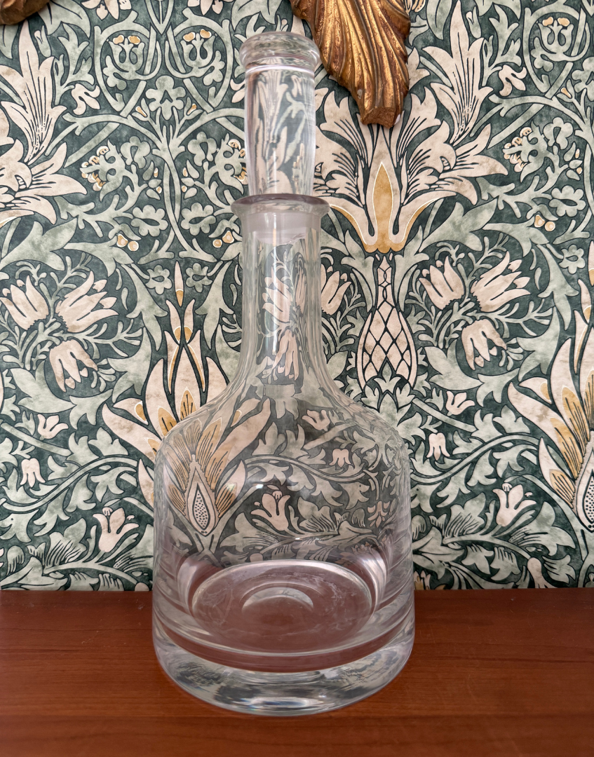 Decorative glass decanter with intricate patterns against a patterned wallpaper background