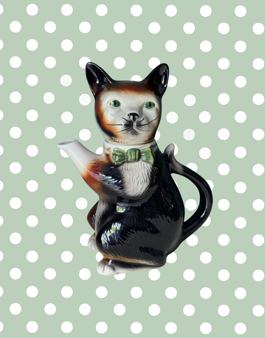 A vintage Tony Wood Staffordshire pottery teapot shaped like a tuxedo cat with a green bow tie.