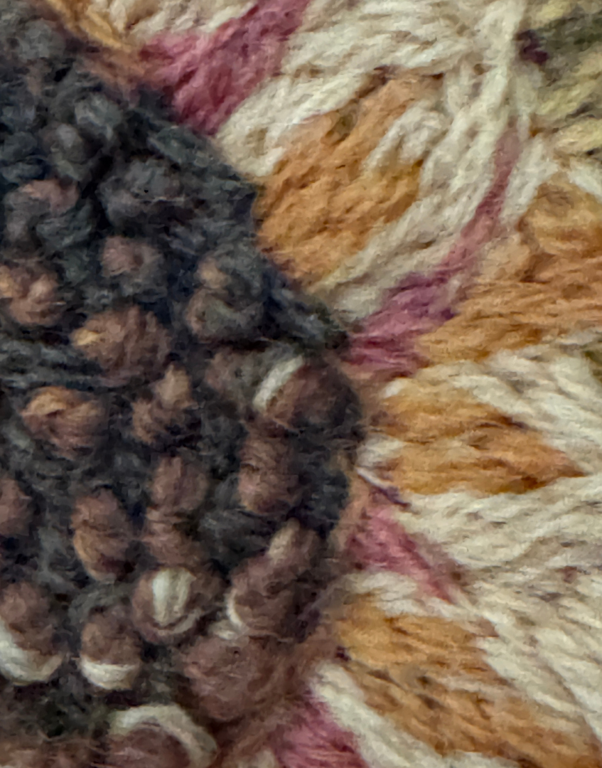 Close up of densely worked French knot stitching forming the centre of an embroidered sunflower on the antique pelmet.