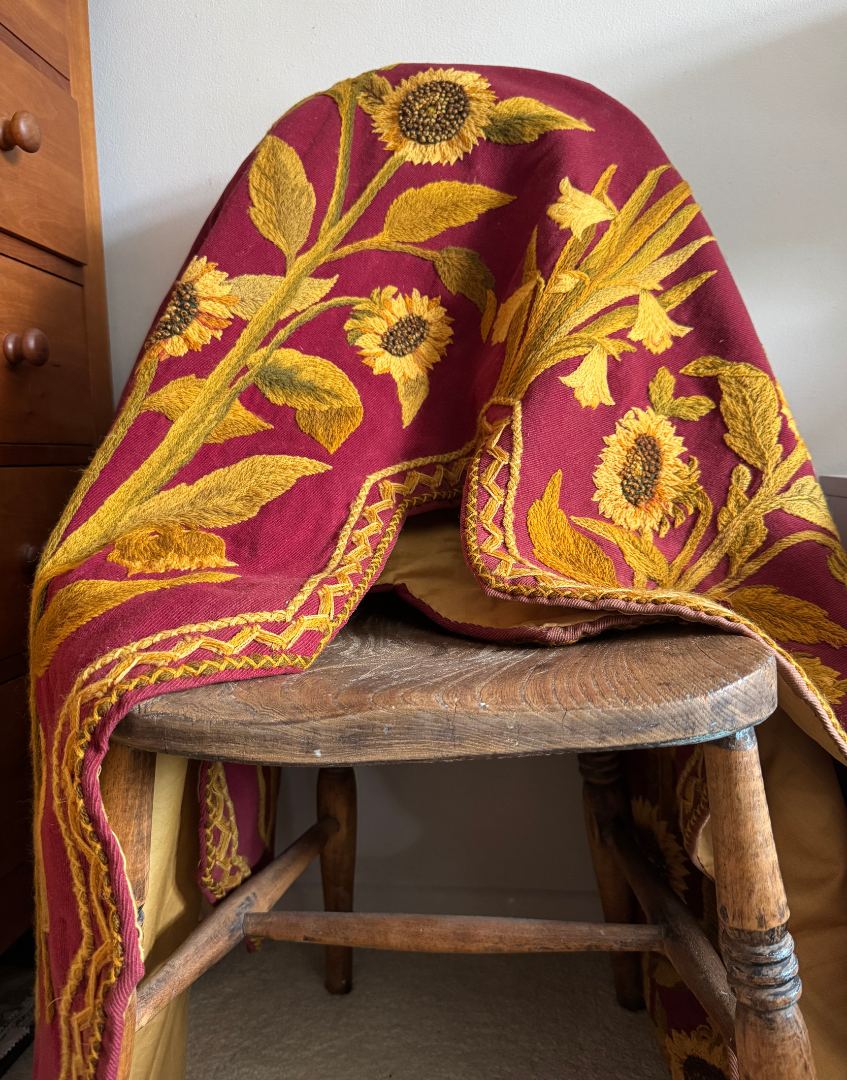 Close view of an antique Arts and Crafts pelmet draped over a traditional chair, highlighting the tactile crewelwork and deep plum textile.