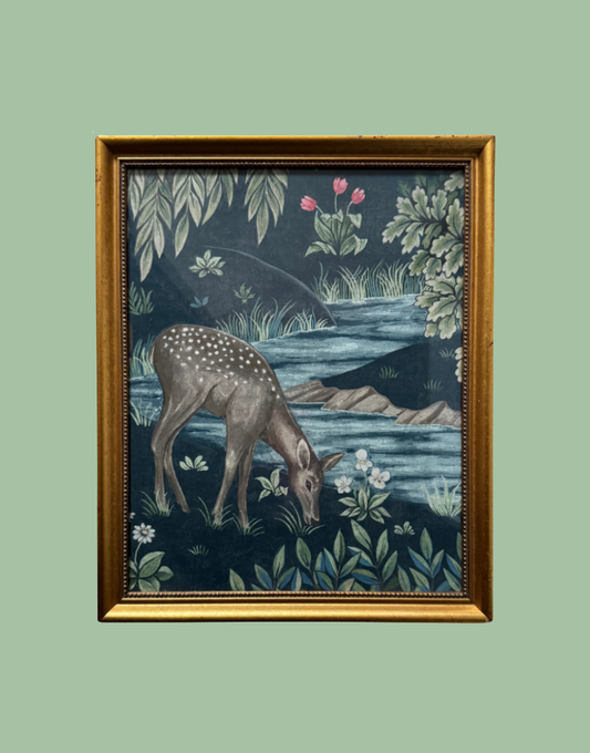 A framed William Morris art print depicting a spotted deer grazing by a river, with a dark blue background and green foliage, enclosed in a gold frame.