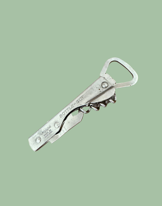 A vintage silver metal bottle opener with a corkscrew attachment, featuring the engraved brand name 'Bottle Boy' and 'Corksmith & Son'.