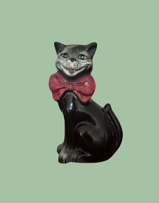 A glossy black cat decanter figurine wearing a large pink bow tie.