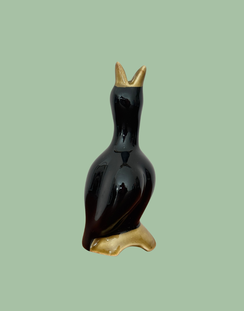 Side view of the vintage black pie bird showing its raised open beak, rounded body and earthy olive log base.