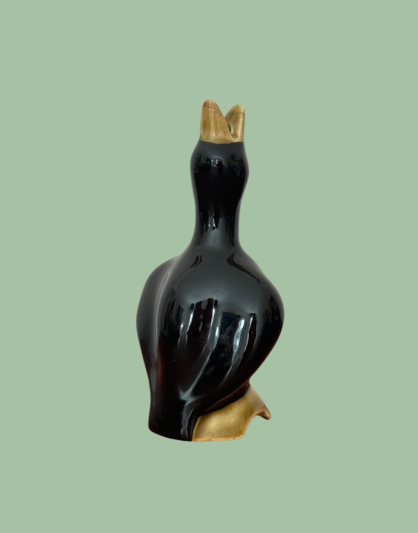 Vintage glossy black ceramic pie bird with an open olive-toned beak and moulded log base against a sage background.