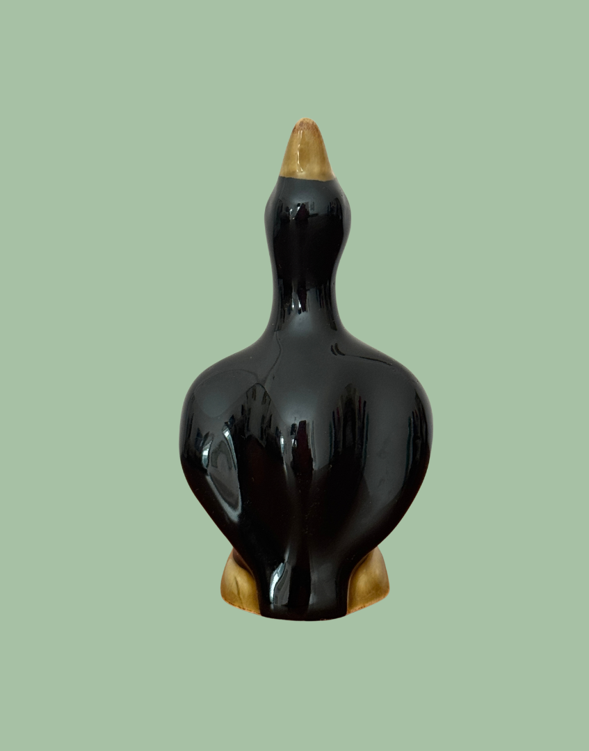 Rear view of the vintage pie bird showing its glossy black back, moulded wings and tapered tail above the log base.