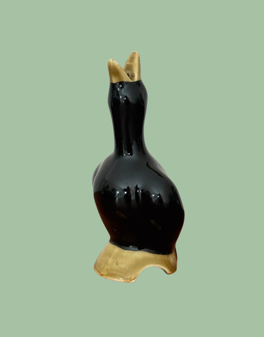 Side view of the black ceramic pie bird showing its curved body, moulded wing and arched opening in the olive-toned log base.