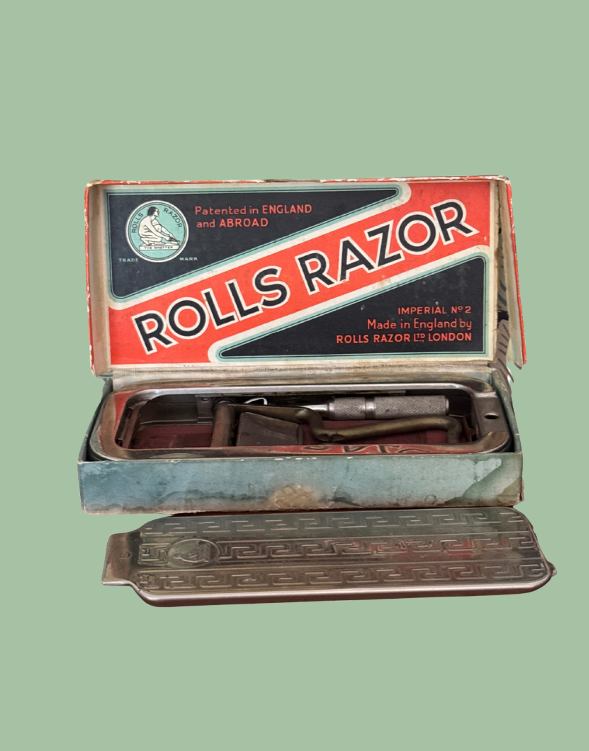 Vintage Rolls Razor men's grooming kit shown open, featuring a metal tin with a red, white, and blue label, a small mirror, and a metal tray with a matching rectangular razor resting on top.