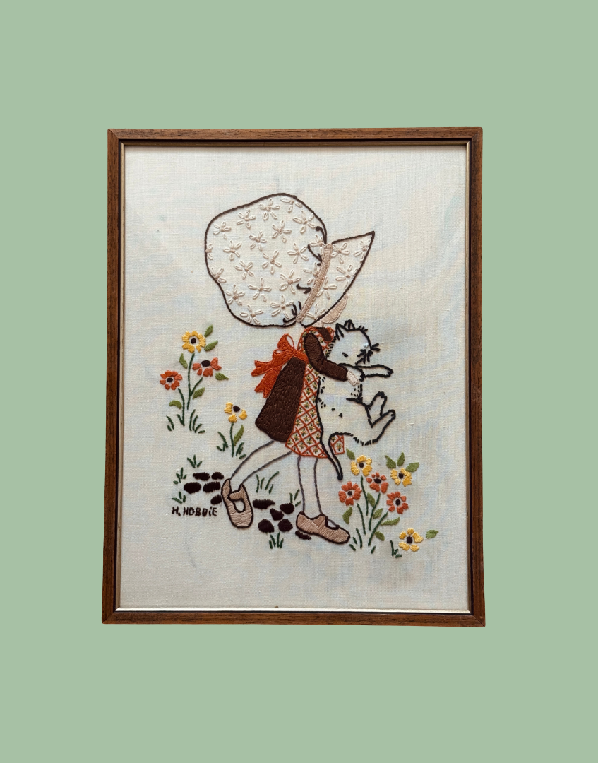 Vintage Hollie Hobbie framed embroidery featuring girl holding white cat with floral background.