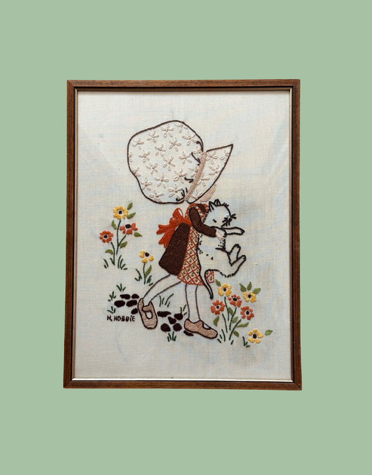 Vintage Hollie Hobbie framed embroidery featuring girl holding white cat with floral background.
