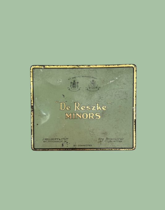 A vintage rectangular tin of 'De Reszke' Minors cigarettes, featuring a distressed sage green background with gold lettering and a gold border, set against a solid light green backdrop.