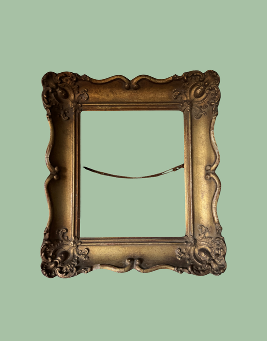An ornate vintage-style picture frame with a distressed gold finish, shown from the back against a solid sage green background.