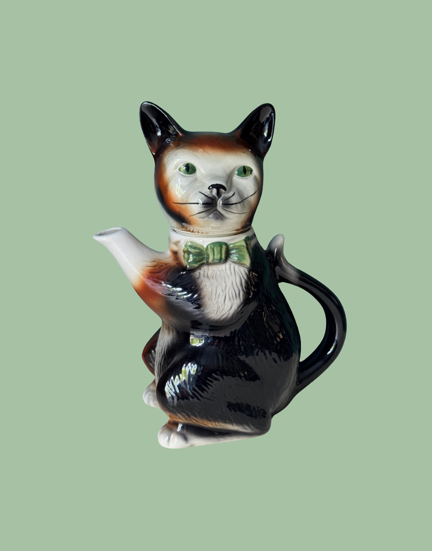 A vintage Tony Wood Staffordshire pottery teapot shaped like a tuxedo cat with a green bow tie.