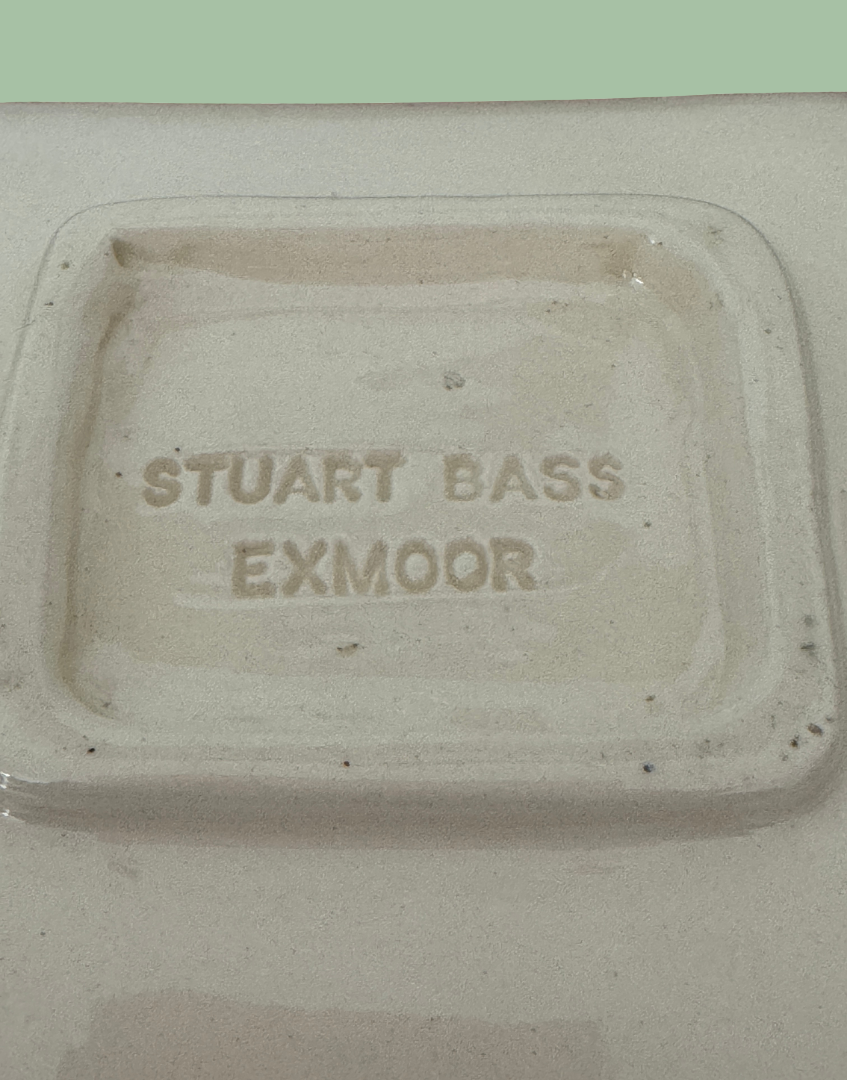 Close-up of the bottom of a ceramic dish or tray with the embossed text 'STUART BASS EXMOOR' visible on a speckled off-white surface.