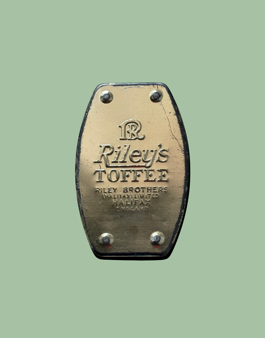 A vintage brass-toned metal plate with rounded corners and four rivets, embossed with the text 'Riley's TOFFEE' and 'RILEY BROTHERS MANHATTIN, PA., U.
