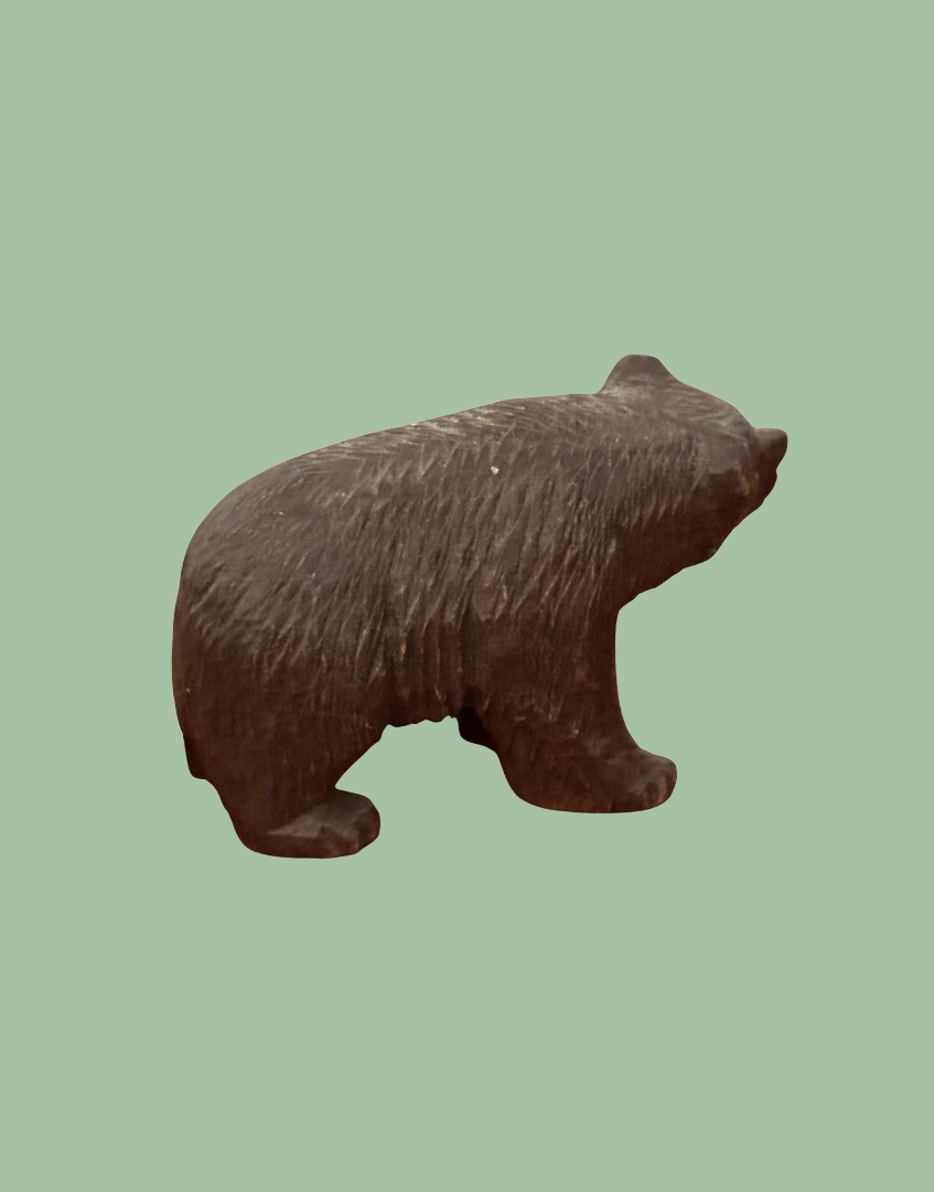 A carved brown bear figurine shown from the side against a solid light green background.