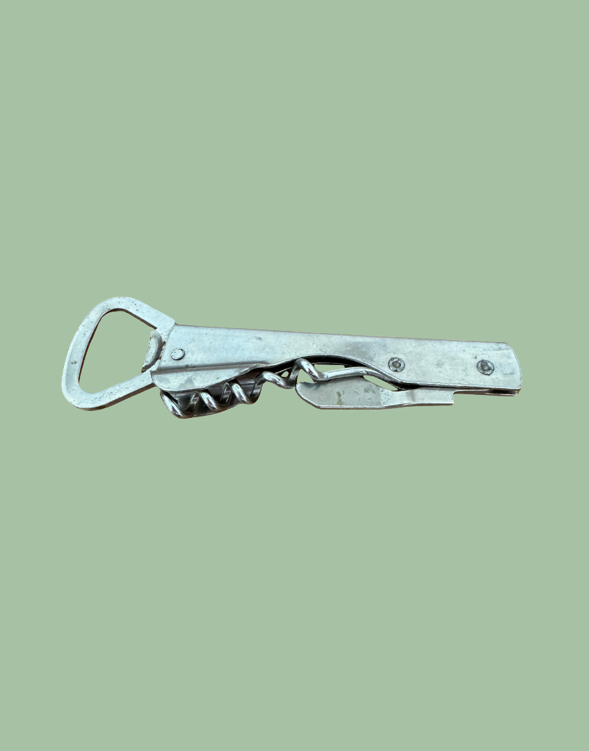 A vintage silver metal multi-tool bottle opener with a twisted center screw, shown against a solid sage green background.
