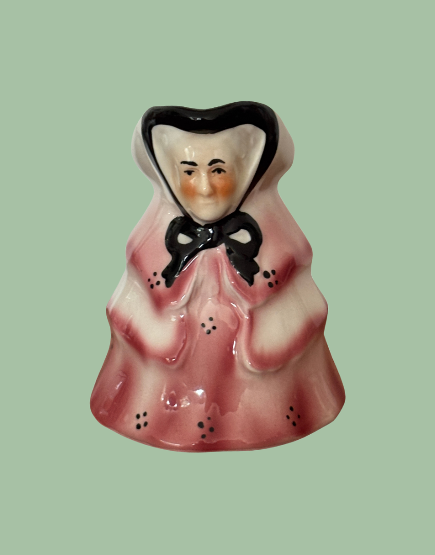 Small ceramic milk jug of a an old lady in a pink dress with a black bow 